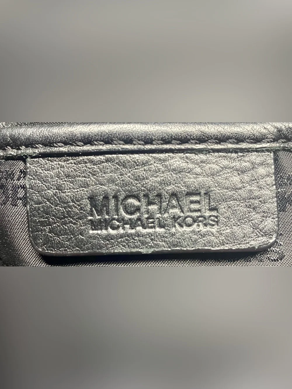 Michael Kors black leather handbag features a prominent gold circular logo charm
